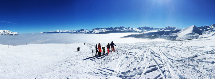 People skiing on snowcapped mountain against blue sky