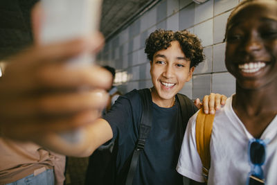 Happy teenage boy taking selfie with male friend through smart phone in underground tunnel