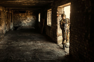 Young soldiers with guns, a soldier in equipment and with arms inspects a ruined house outside the