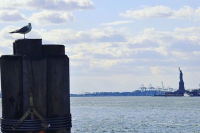 Bird perching on statue by sea against sky