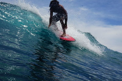 Low section of man surfing in the ocean against sky