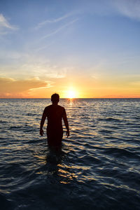 Rear view of silhouette man on sea against sky during sunset