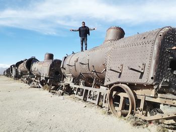 Man with arms outstretched standing on abandoned train 