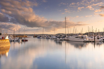 Sailboats moored at harbor against sky during sunset