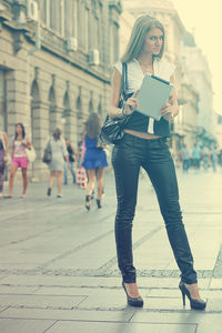 Portrait of beautiful woman holding digital tablet while standing on city street