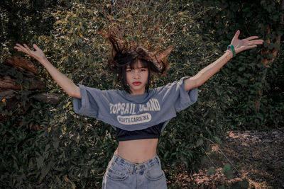 Portrait of woman with arms raised standing by plants outdoors