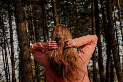 Rear view of woman standing by tree trunk in forest