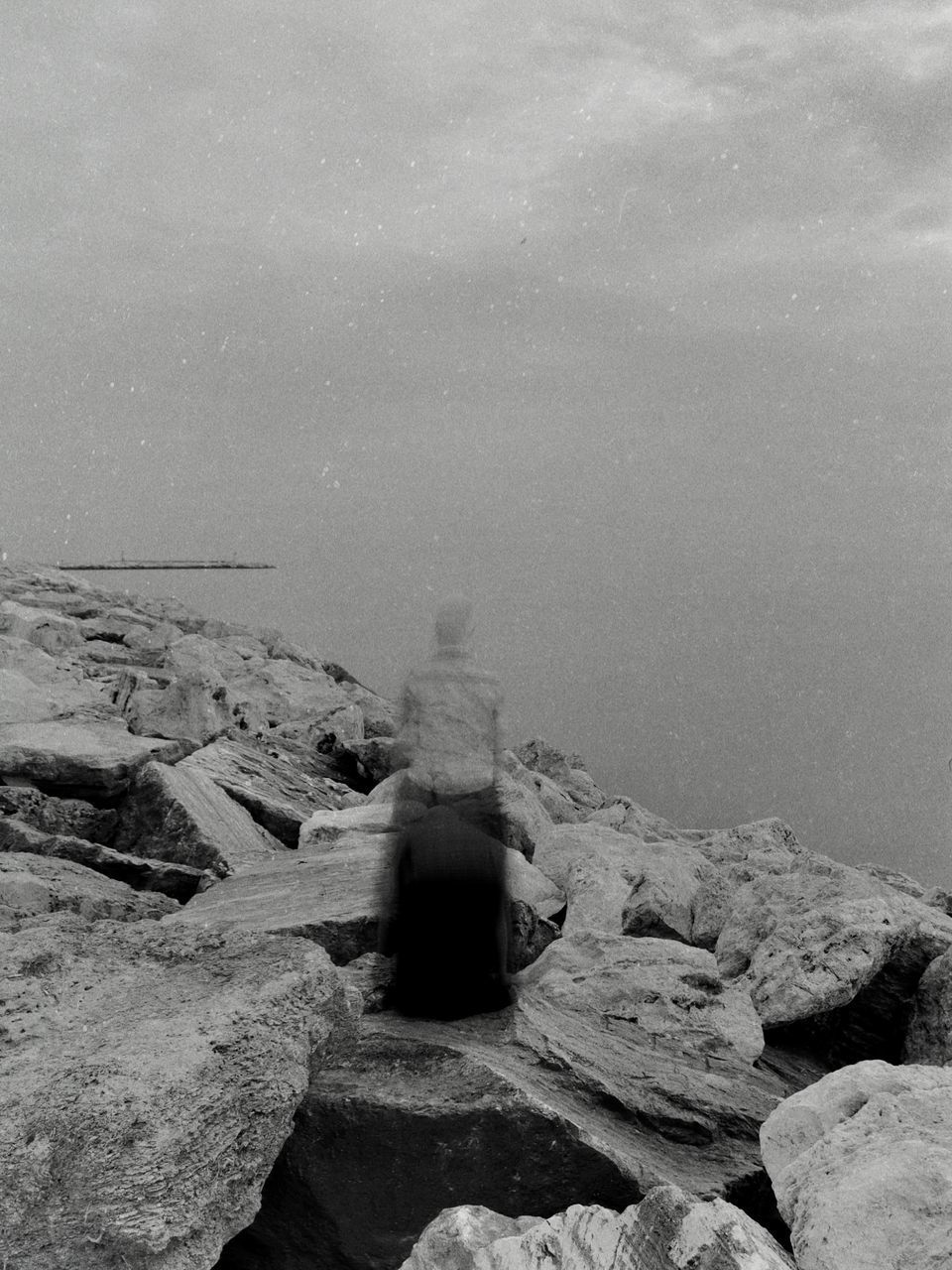 REAR VIEW OF ROCK SITTING ON ROCKS BY SEA