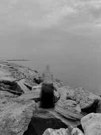 Rear view of rock sitting by sea against sky