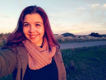 Portrait of smiling young woman on field during sunset