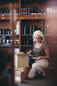 Senior saleswoman reading paper while unpacking box in deli