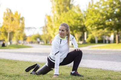 Focused paralympic female runner with leg prosthesis stretching body and doing forward bend during training