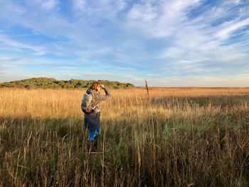 Rear view of a woman walking in the morning sun through a reed land under a blue sky