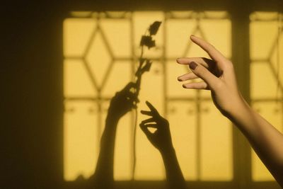 Cropped hand of woman gesturing against shadows on yellow wall