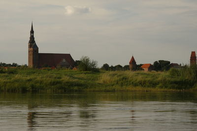 Built structure by lake and buildings against sky