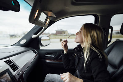 Side view of girl applying lipstick while sitting in car