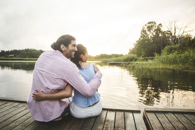 Rear view of couple sitting on lake against sky