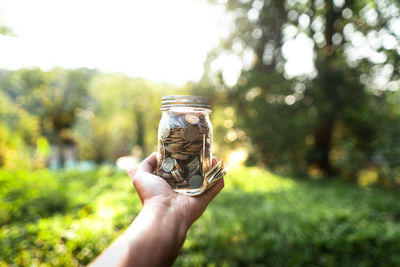 Midsection of person holding jar against trees