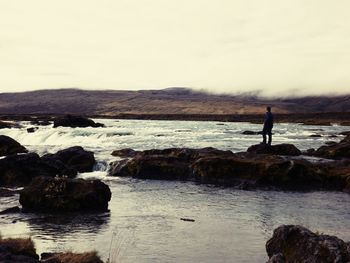 Silhouette woman standing on rock by sea against sky