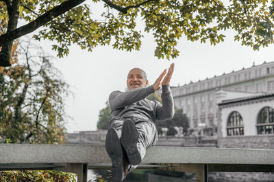 Elderly man sitting on a bench by the river, smiling and clapping hands happily