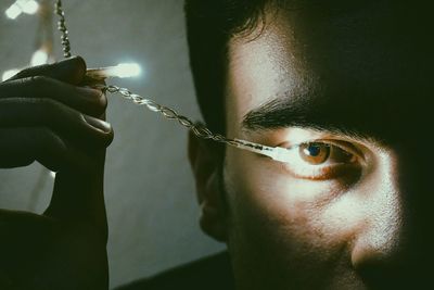 Cropped eye of man with illuminated string light in darkroom