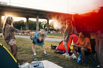 Happy friends performing limbo dance on lawn at music festival during summer