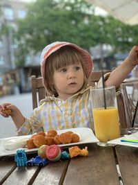 A little girl wearing a summer hat eating cheese balls and drinking orange juice at summer terrace