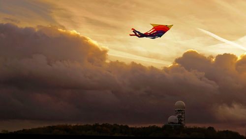 Low angle view of kite flying against cloudy sky during sunset