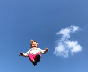 Low angle view of girl jumping against blue sky