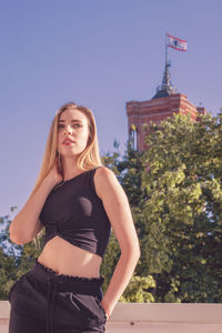 Thoughtful young woman standing on balcony against clear blue sky