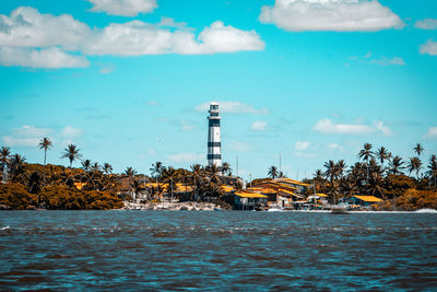 Lighthouse amidst buildings and sea against sky