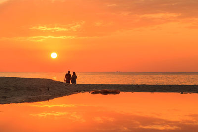 Silhouette people on beach against orange sky