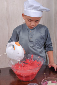 Boy mixing batter in bowl on table at home