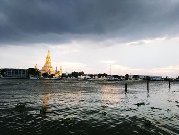 View of buildings by river against cloudy sky