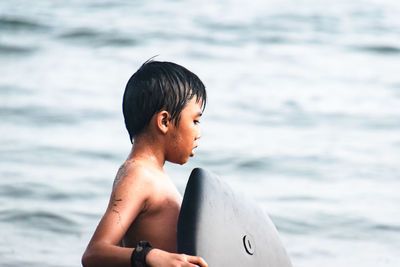 Shirtless boy with surfboard on beach