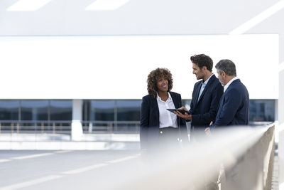 Male entrepreneur with digital tablet having discussion while standing at office building terrace