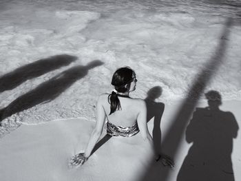 Woman sitting on sea shore amidst shadow at beach