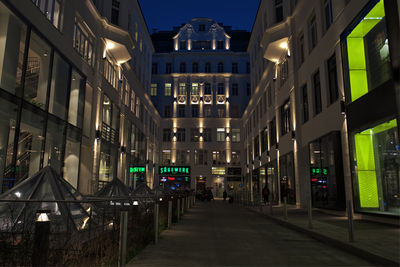 Illuminated street amidst buildings in city at night