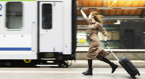 Side view of woman running behind train at railroad station