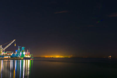 Illuminated city by sea against sky at night