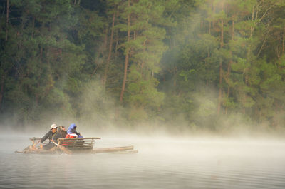 People in boat on river against trees