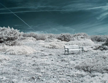 Empty bench on snow covered land against sky