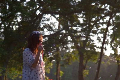 Woman blowing bubbles against trees