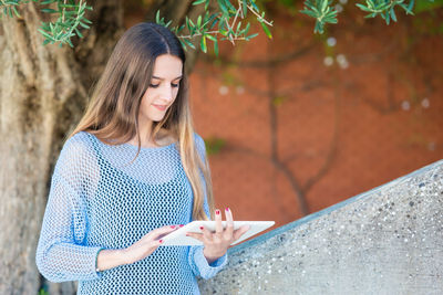 Smiling woman using digital tablet against tree