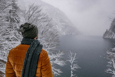 Rear view of man looking at lake during snowfall