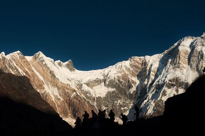 Low angle view of snowcapped mountains against clear blue sky