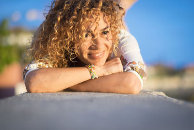 Smiling woman with curly hair lying down on retaining wall