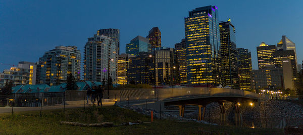 Calgary's iluminated cityscape and river bridge at dusk.