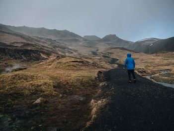 Rear view of man walking on mountain against sky