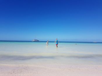 Boy and girl on beach against clear blue sky